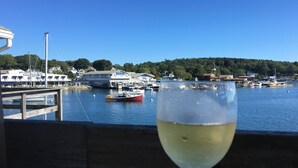 A glass of white wine on a wooden deck overlooking a marina with boats and a building named "South Shore Inn". - Gorgeous Views of Harbor Entrance! Walk to town, east side location. (Boothbay Harbor)