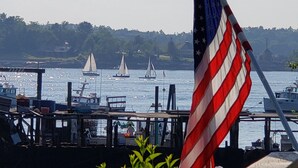 A marina with several sailboats, an American flag, and a dock with various structures. - Gorgeous Views of Harbor Entrance! Walk to town, east side location. (Boothbay Harbor)