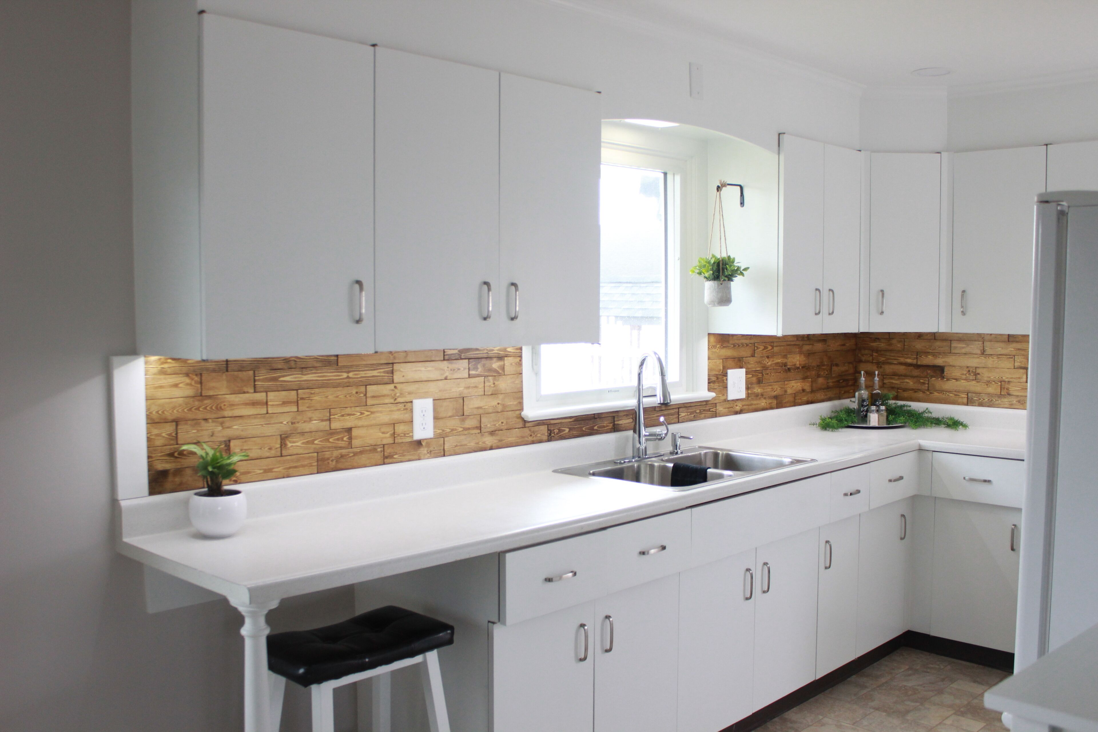 Una cocina moderna con armarios blancos, un protector contra salpicaduras de madera, un lavamanos de acero inoxidable y una pequeña planta en maceta.
