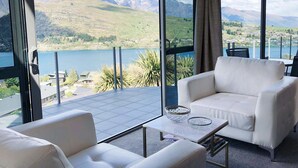 Une pièce moderne avec un canapé et un fauteuil blancs, une table basse en verre et une vue sur un lac et des montagnes.