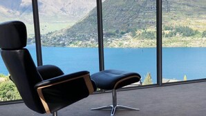 Un fauteuil moderne avec un siège en cuir noir et des éléments décoratifs en bois, placé devant de grandes fenêtres donnant sur un lac et des montagnes.