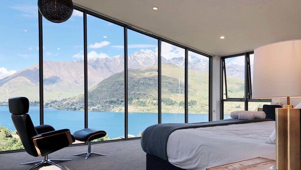 Une chambre avec un grand lit, une chaise, une table de chevet et une vue sur les montagnes et un lac.