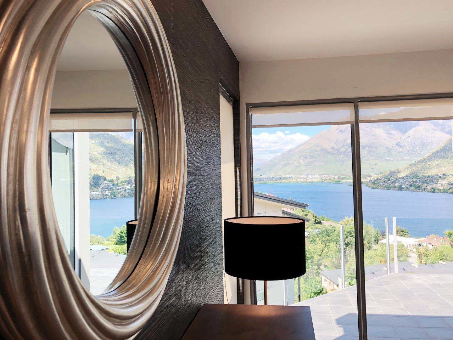 A room with a large mirror, a lamp, and a view of a lake and mountains.