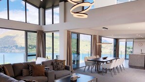 Un vaste espace de vie comprenant un canapé, une table basse et une table à manger, ainsi que de grandes fenêtres offrant une vue sur un lac et des montagnes.