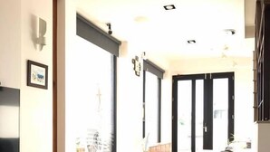 A modern living room with a white sofa, a flat-screen TV mounted on the wall, and a large window providing natural light. - Simple Life Home Stay (Magong)
