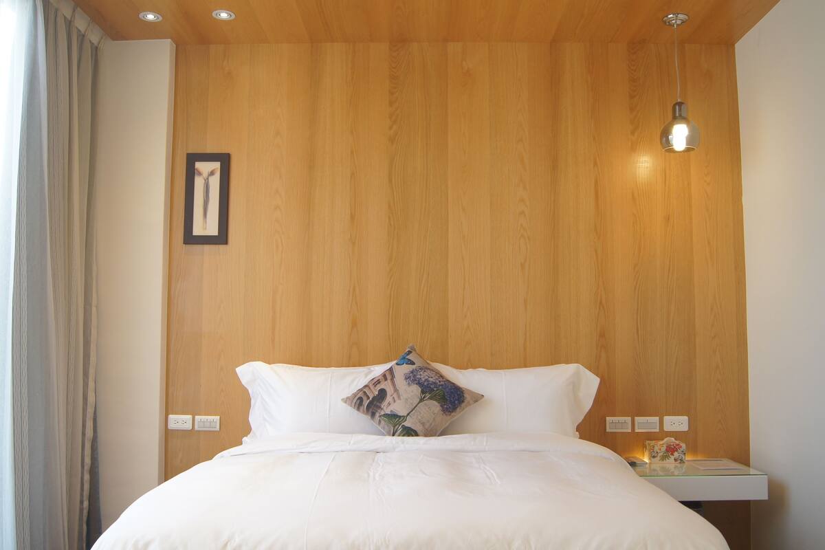 A neatly made bed with white linens, a wooden headboard, and a single decorative pillow.
