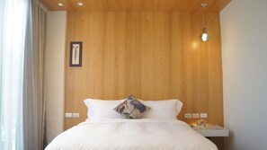 Una cama bien hecha con sábanas blancas, un cabecero de madera y una única almohada decorativa.