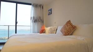 A hotel room with a large bed, a view of the sea, and a window with sheer curtains. - Simple Life Home Stay (Magong)