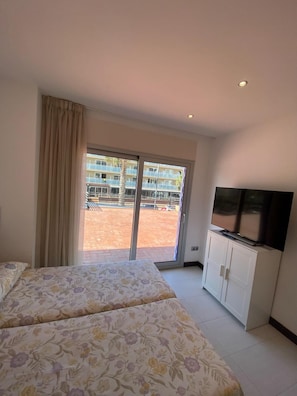 A hotel room with a bed, a TV, and a sliding glass door leading to an outdoor area.