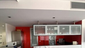 Una cocina moderna con armarios blancos, una pared de acento roja y una zona de comedor con mesa y sillas de vidrio.