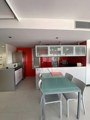 A modern kitchen with white cabinets, a red accent wall, and a dining area with a glass table and chairs. - APARTMENT 7 ADULTS (L'Estartit)