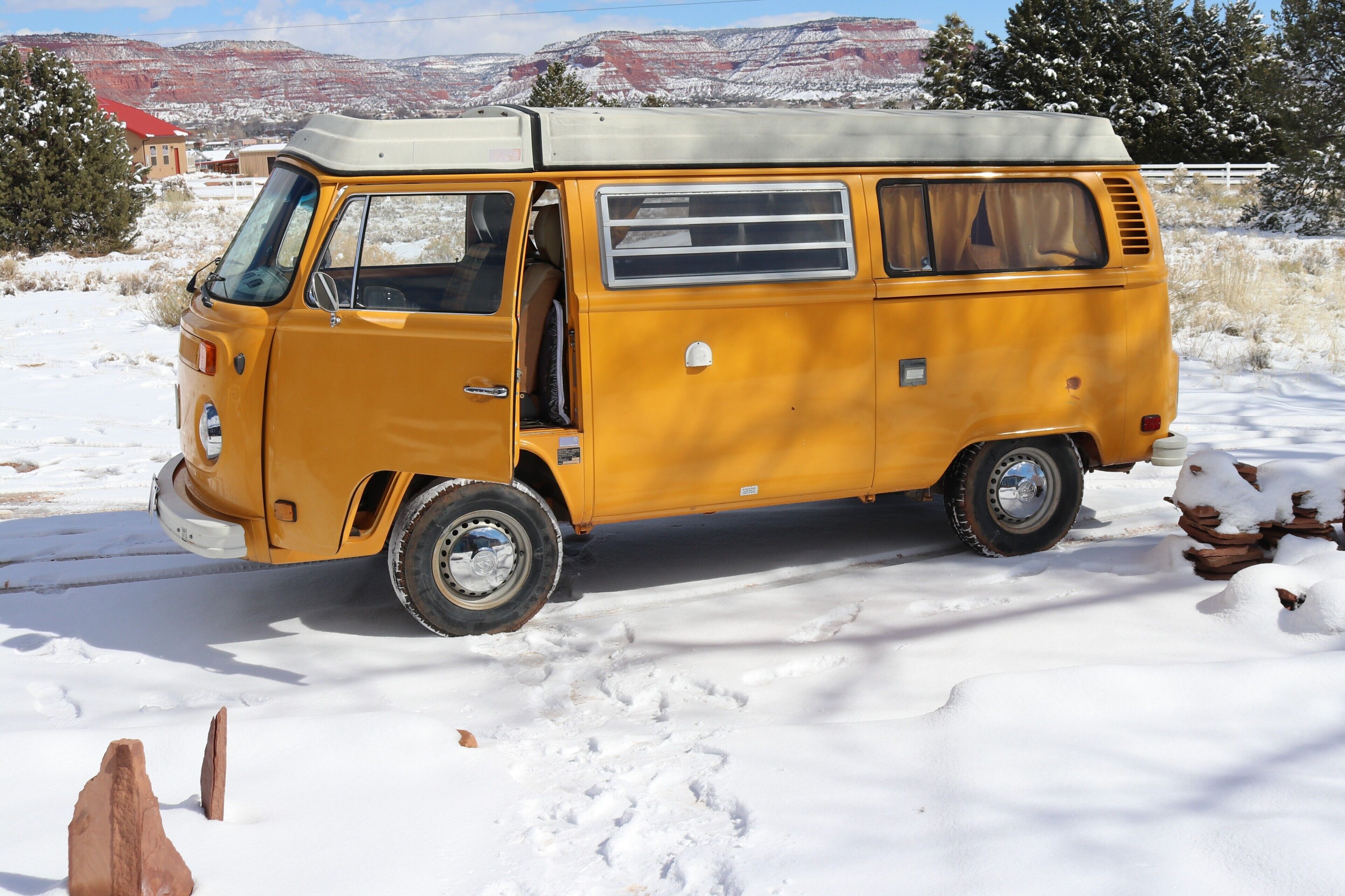 A yellow van parked in a snowy area with a mountainous background.