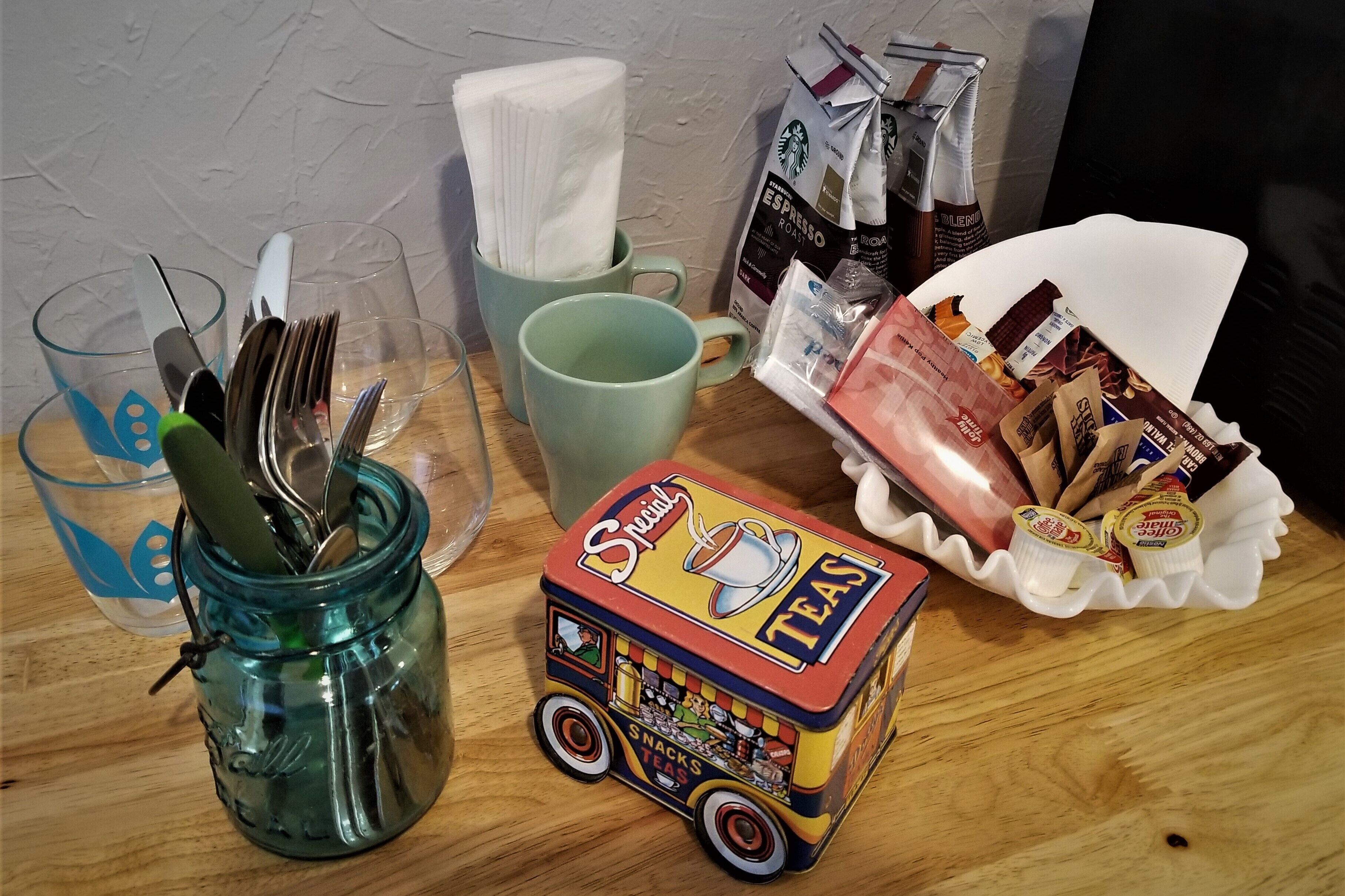 Eine Küchenarbeitsplatte mit einem grünen Glas, einer Tasse, einem kleinen Spielzeug-Foodtruck und einer Korb voller Snacks.