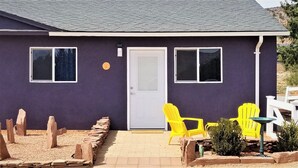 A house with a purple exterior, a white door, and two windows. There are yellow chairs and a small garden area with rocks and plants. -  Quiet and Solitude with Magnificent Patio View (Kanab)