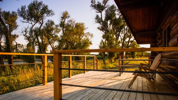 Une terrasse en bois avec une rambarde donnant sur une étendue d’eau et des arbres.