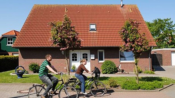 Une maison à deux étages, avec un toit recouvert de tuiles rouges, une porte d’entrée et une petite fenêtre.