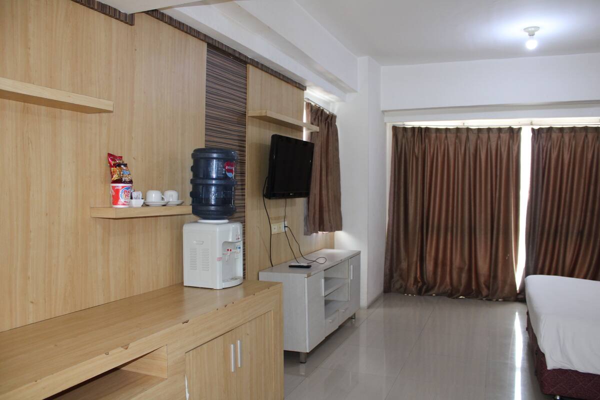 A hotel room with a wooden cabinet, a water dispenser, a television, and a bed.