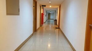 A clean, well-lit hotel corridor with a shiny tiled floor, wooden doors, and a red fire extinguisher. - Sun Apartment Semarang (Semarang)