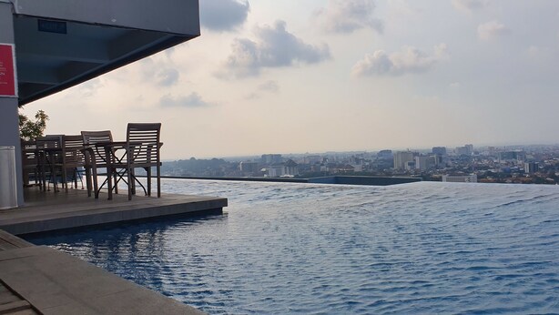An infinity pool with wooden chairs and a cityscape view. - Sun Apartment Semarang (Semarang)