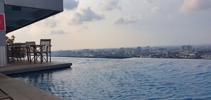 An infinity pool with wooden chairs and a cityscape view. - Sun Apartment Semarang (Semarang)