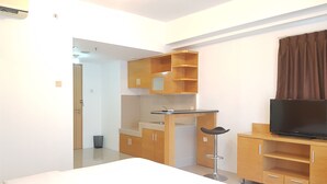 A modern hotel room with a bed, a TV, wooden cabinets, a small kitchen area, and a bathroom visible through an open door. - Sun Apartment Semarang (Semarang)