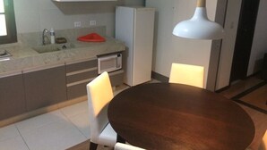 Ett kompakt kök med mikrovågsugn, kylskåp, diskho och en matplats med bord och stolar.