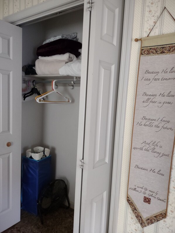 A closet with hanging clothes, a blue storage bin, and a fan.