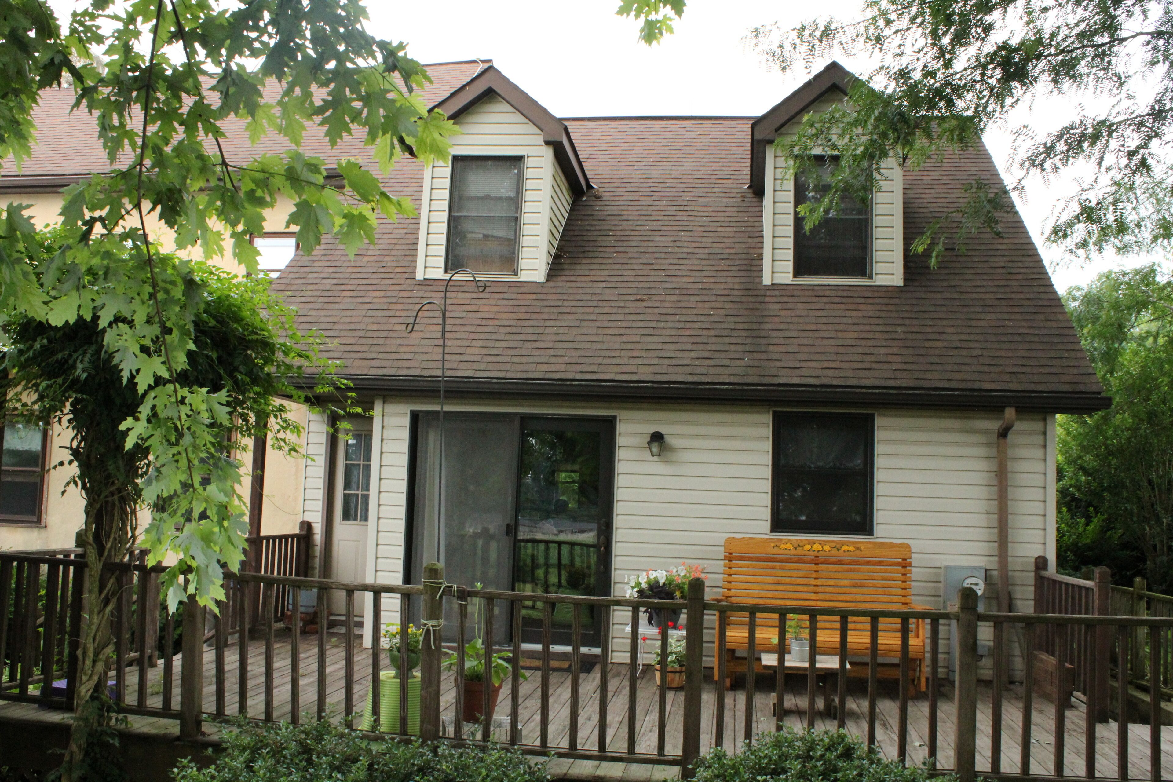 A two-story house with a porch, a wooden bench, and potted plants.