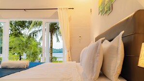 A hotel room with a bed, a view of greenery and water outside, and a curtain. - The Hawk's Nest Resort (Sabang)