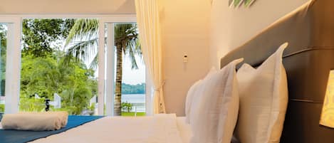 A hotel room with a bed, a view of greenery and water outside, and a curtain.