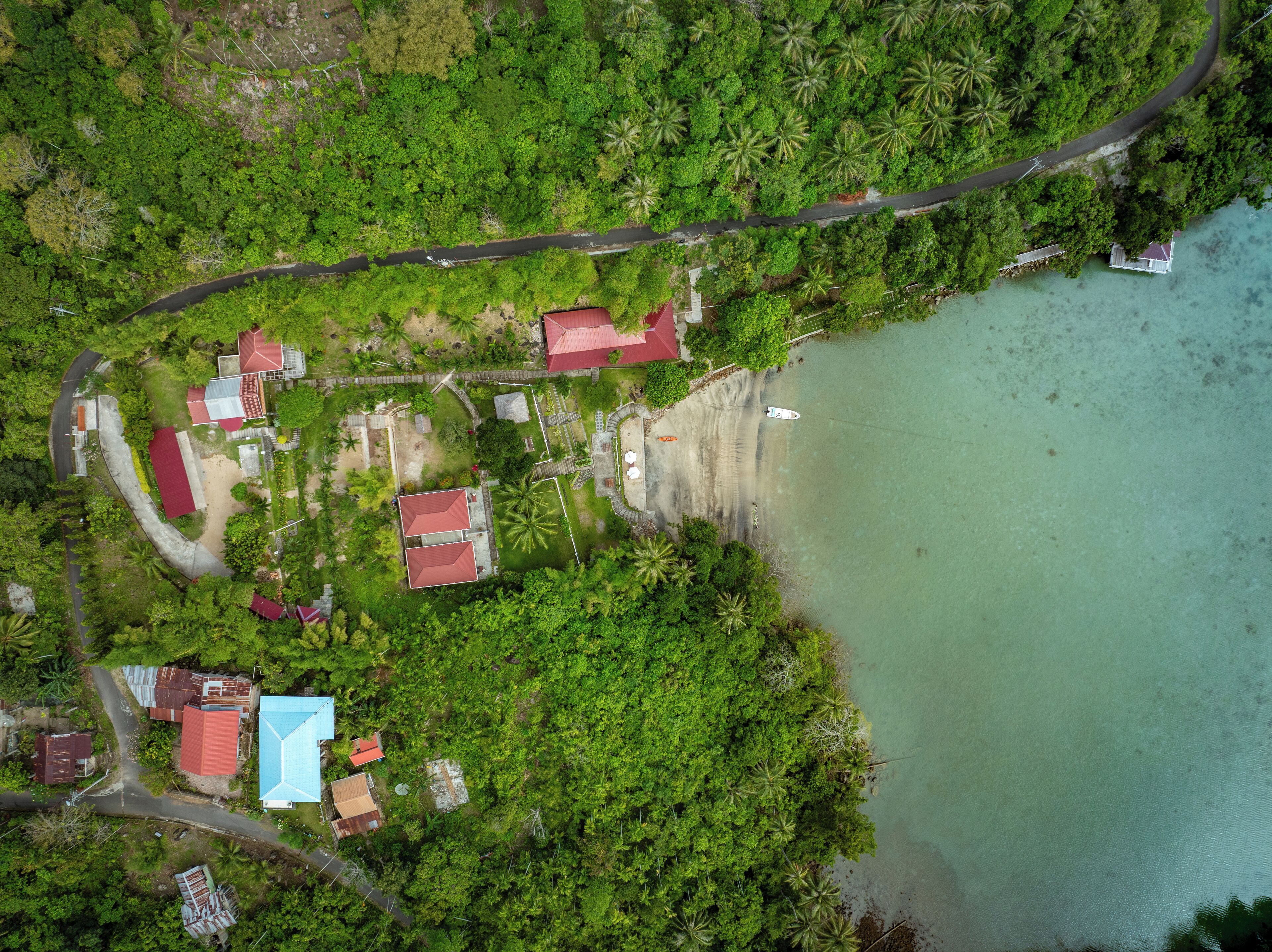 An aerial view of a coastal area with a road, several buildings with red roofs, and a beach.