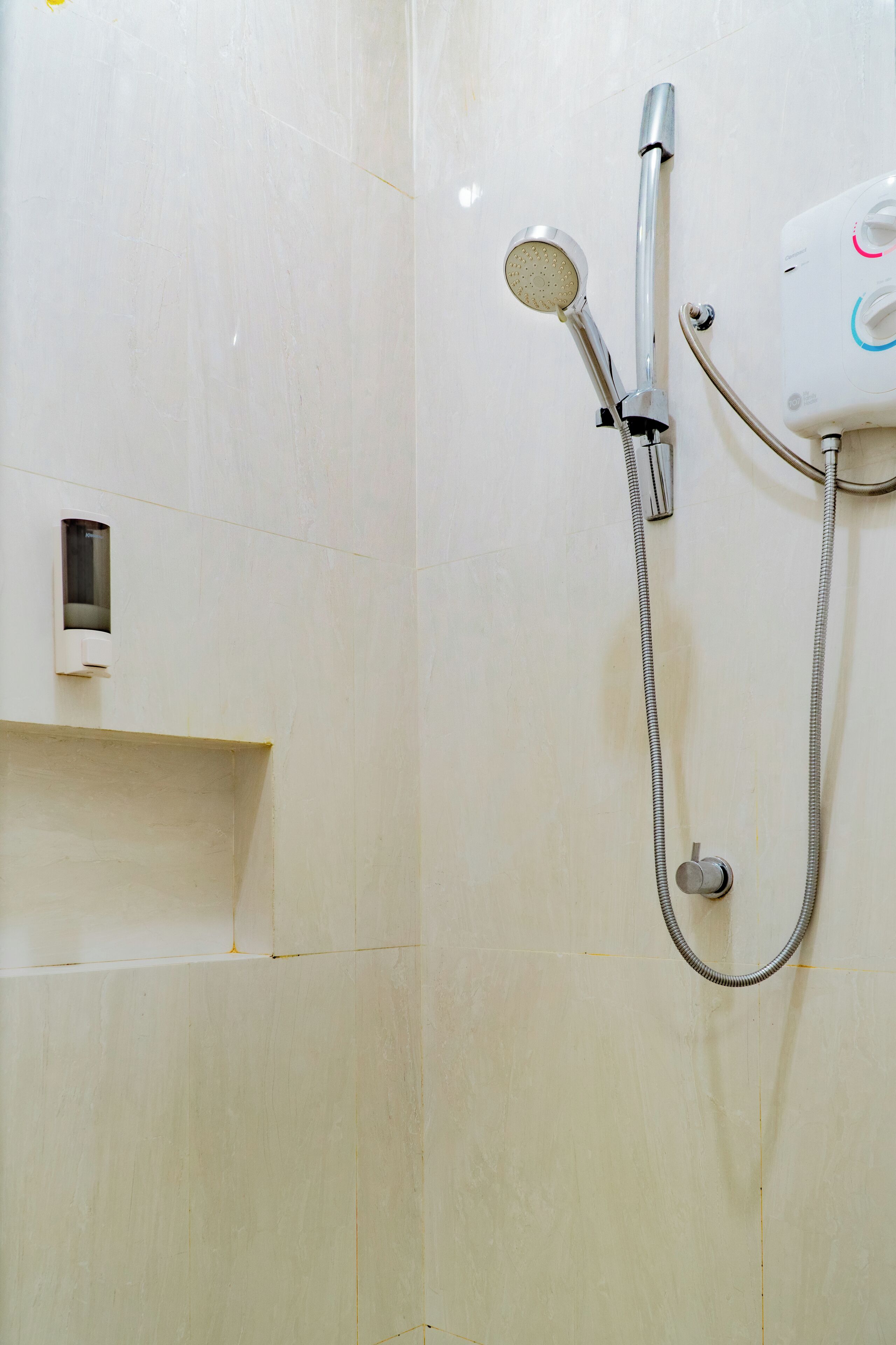 Une douche équipée d’un pommeau de douche à main et d’un panneau de commande fixé au mur.
