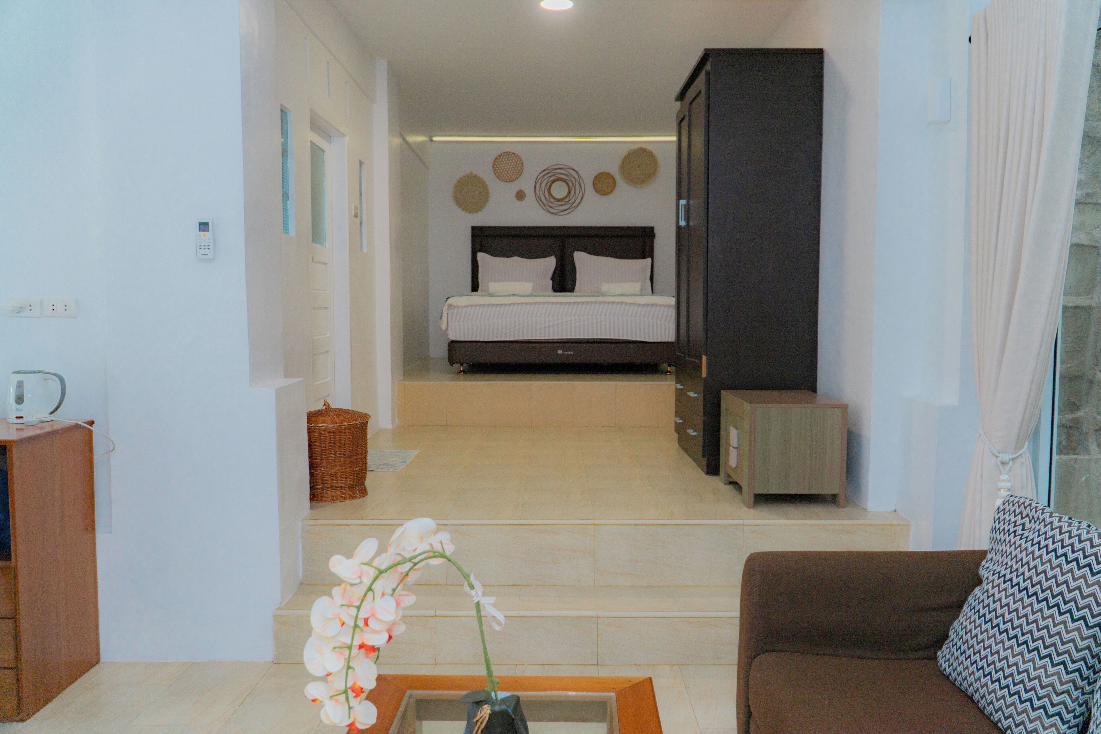 A hotel room with a bed, a sofa, a small table with a vase of flowers, and a wall-mounted control panel.