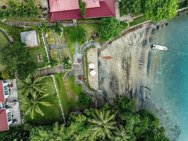 An aerial view of a beachfront property with a swimming area, a small dock, and a pathway leading to a building with a red roof. - The Hawk's Nest Resort (Sabang)