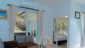 A living room with a brown sofa, a glass coffee table, and a view of a bedroom through glass doors. - The Hawk's Nest Resort (Sabang)