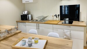 Una cocina moderna con microondas, tostadora y pileta. Hay una mesa de madera con una bandeja de tazas y un tarro de vidrio.