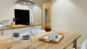 Una cocina moderna con una campana de acero inoxidable, un televisor de pantalla plana negro y una encimera de madera. Hay una bandeja con tazas y una botella en la mesa.