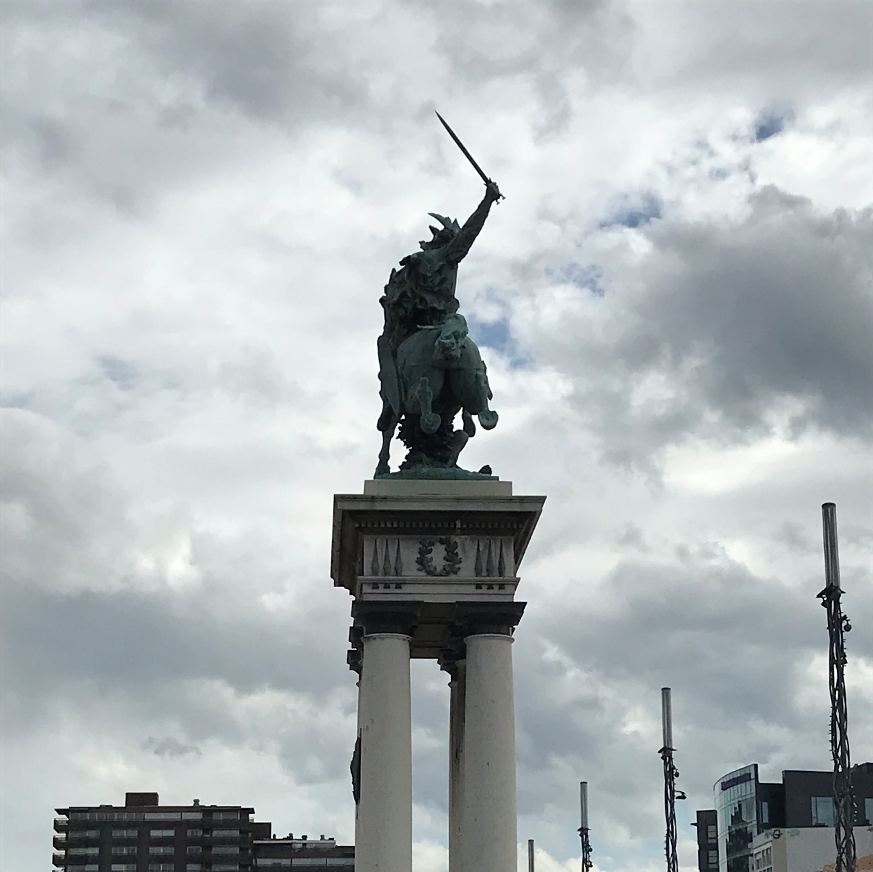 A statue on a pedestal with a cloudy sky in the background.