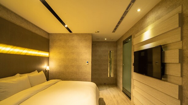 Una habitación de hotel moderna con una cama grande, un televisor de pantalla plana en la pared y un vestidor.