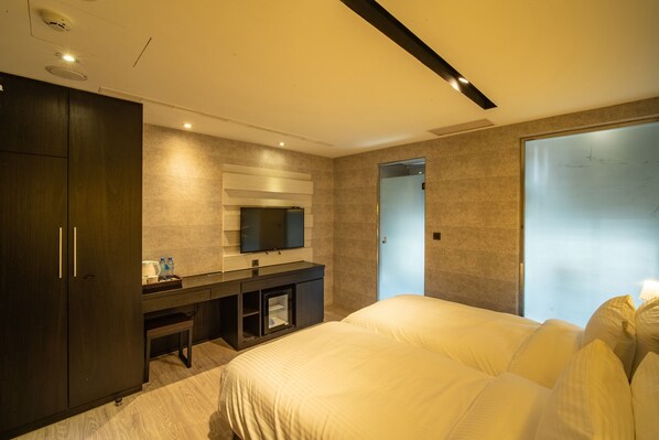 A modern hotel room with a large bed, a TV mounted on the wall, a dark wooden wardrobe, and a small desk with a mirror. - Hotel Bell (Taichung)