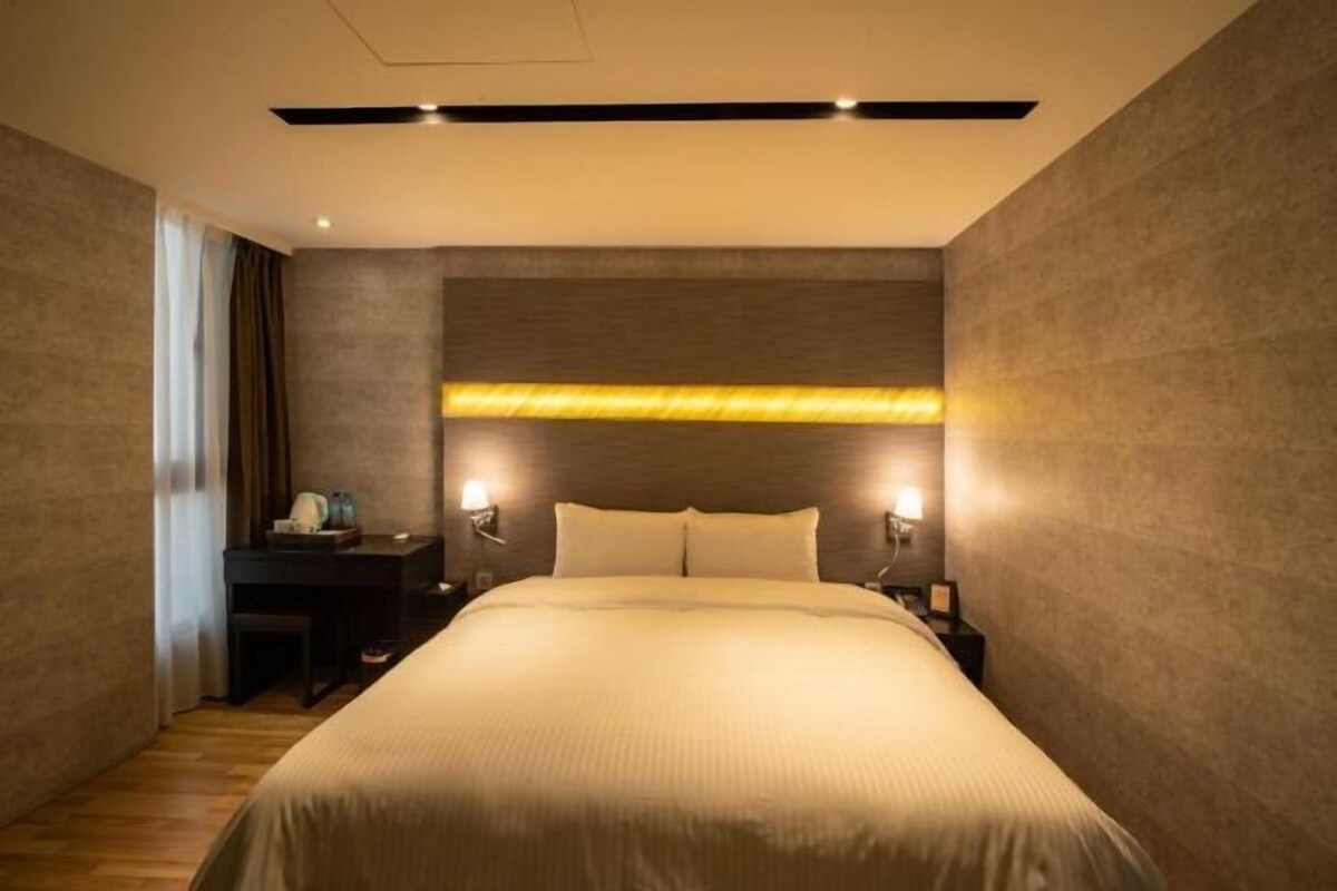 A modern hotel room with a large bed, bedside tables, and a headboard with integrated lighting.