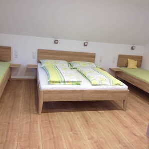 Une chambre avec un grand lit, deux petits lits, un plancher en bois et des murs blancs.