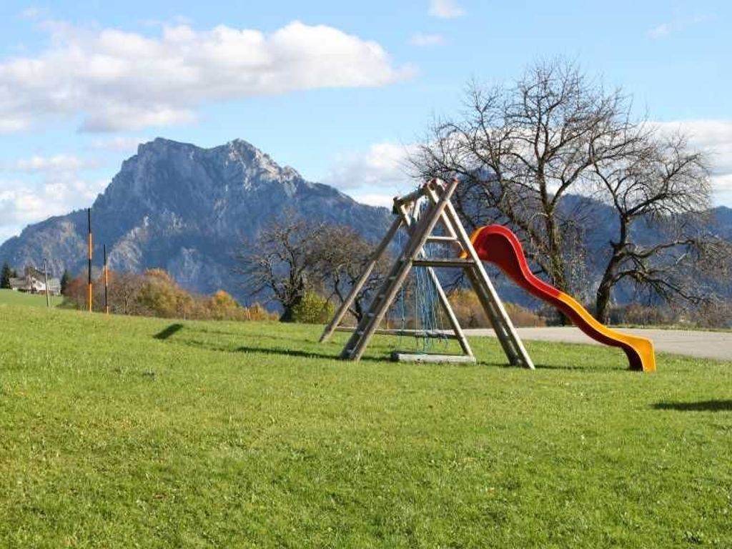 A playground with a slide and swings in a grassy area with mountains in the background.