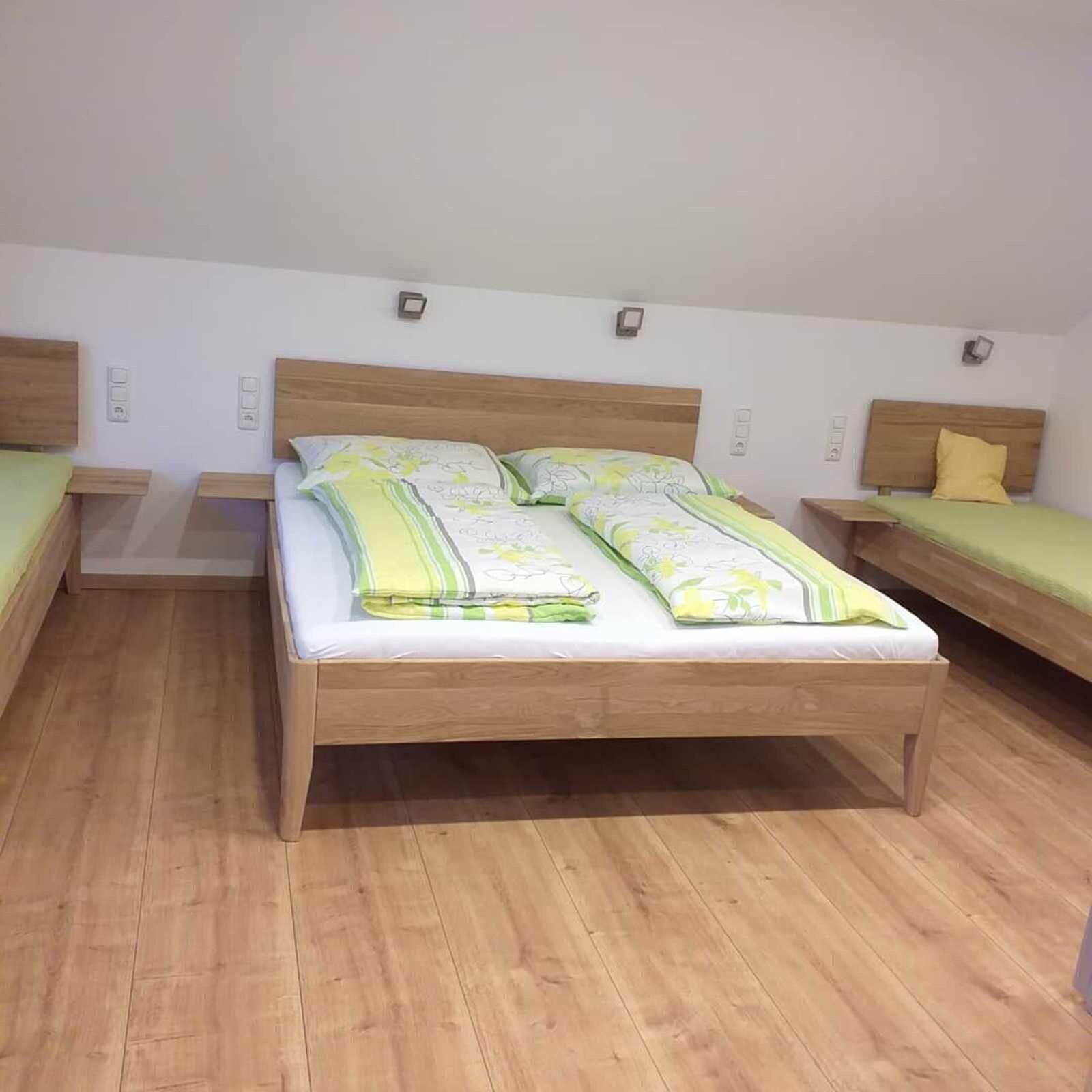 A room with a central bed, two smaller beds, wooden flooring, and white walls.