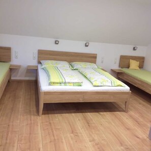 Ein Zimmer mit einem Doppelbett, zwei Einzelbetten, Holzboden und weißen Wänden.