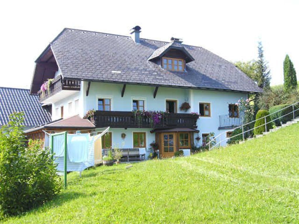 Ein zweigeschossiges Haus mit einem geneigten Dach, einem Balkon mit Blumenkästen und einer Haustür mit einer kleinen Veranda.