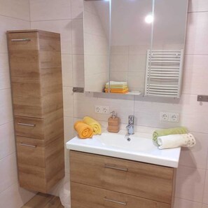 A bathroom with a wooden cabinet, a sink with a mirror, and towels. - Minabauer - Apartment 1 (Altmünster am Traunsee)