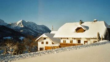 Ein mit Schnee bedecktes Haus mit Bergblick, einer Holzdielen-Terrasse und blauem Himmel.