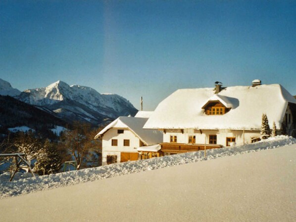 A snow-covered house with a mountain backdrop, a wooden deck, and a clear sky. - Minabauer - Apartment 1 (Altmünster am Traunsee)