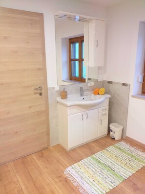 Een badkamer met een houten deur, een witte wastafel met een spiegel erboven en een klein raam.